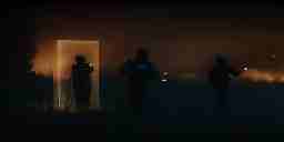 Three soldiers carrying guns walk out of a rectangular gelatinous glowing portal through a forest at night. Portal is amber-colored.