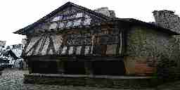 An old Tudor half-timbered building with a worked stone foundation in the middle of a cobblestone town square. A 15th-century house in France.